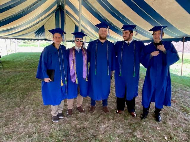Five graduates pose together under outdoor tent
